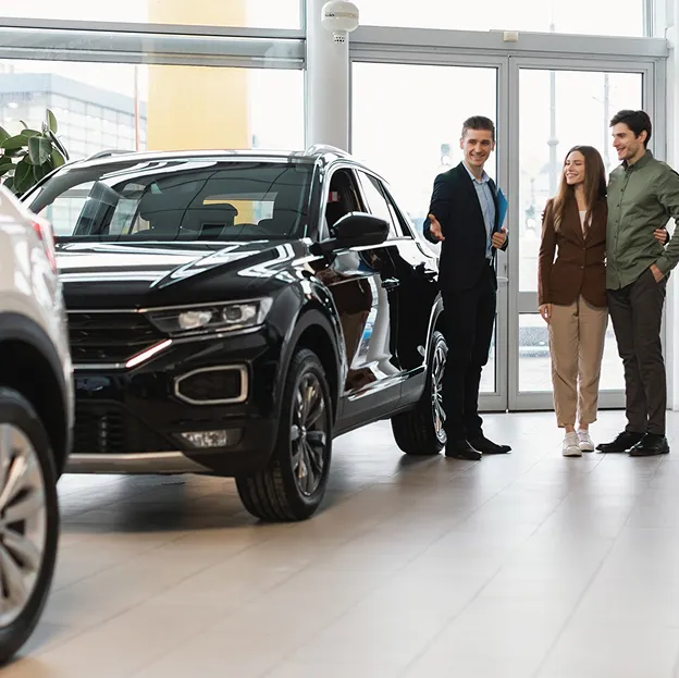 Un concessionnaire montre un SUV noir à un jeune couple souriant dans une salle d'exposition à Poissy dans les Yvelines 78